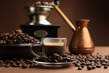 Cup of hot coffee, cezve, grinder and beans on brown background, closeup