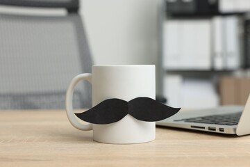 Happy Father's Day. Cup with paper moustache and laptop on wooden table, closeup