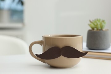 Happy Father's Day. Cup with paper moustache and books on white table indoors, closeup