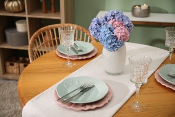 Stylish setting with plates and vase of flowers on wooden table in dining room. Interior design