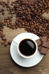 Aromatic coffee in cup, beans and pieces of chocolate on wooden table, flat lay