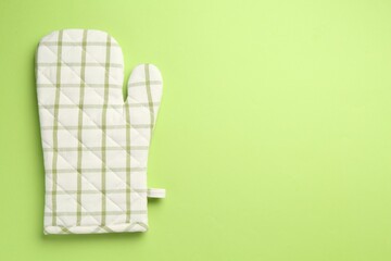 One oven glove on green background, top view. Space for text