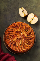 Sponge apple pie with caramelized apples on a green background next to a burgundy kitchen textile...