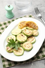 Delicious fried courgette slices with lemon and parsley served on grey table, closeup