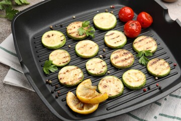 Delicious grilled courgette slices with tomatoes, lemon and parsley in pan on grey textured table, closeup