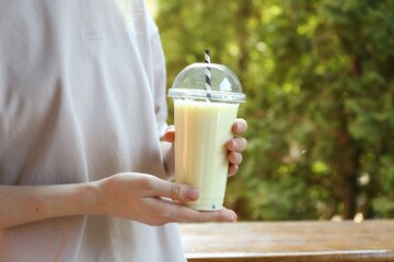 Woman holding tasty milkshake in plastic cup outdoors, closeup