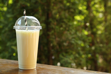 Tasty milkshake in plastic cup on wooden table outdoors, space for text