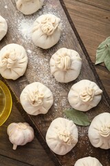 Uncooked khinkalis (dumplings) with flour, garlic and bay leaves on wooden table, flat lay