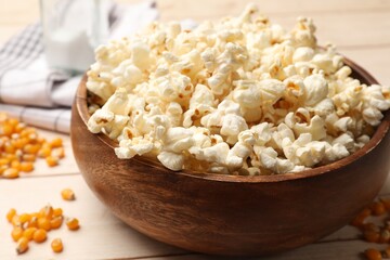 Tasty popcorn and corn kernels on light wooden table, closeup