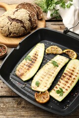 Delicious grilled courgette slices with spices and lemon in pan on wooden table, closeup