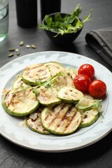 Delicious grilled courgette slices with tomatoes and microgreens on black table, closeup