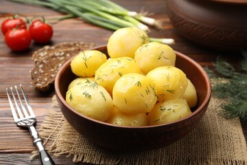 Tasty young boiled potatoes with dill and oil in bowl on wooden table, closeup