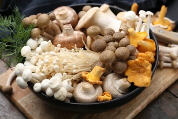 Different raw mushrooms and dill in bowl on wooden table, closeup