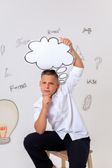 Thoughtful schoolboy in uniform sitting on wooden stool, student portrait with science and math formulas on white background, education and learning concept