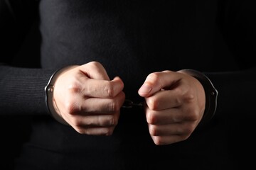 Woman in metal handcuffs on black background, closeup