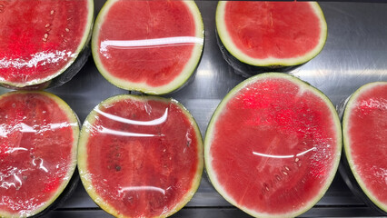 In the fruit section of a supermarket, bright red, sliced watermelons are on display.