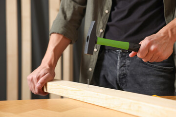 Man hammering nail into wooden plank indoors, closeup