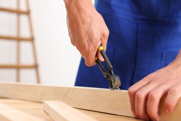 Professional repairman pulling nail out of wooden plank with pincers indoors, closeup