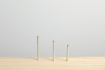 Metal nails in wooden plank on light grey background, closeup