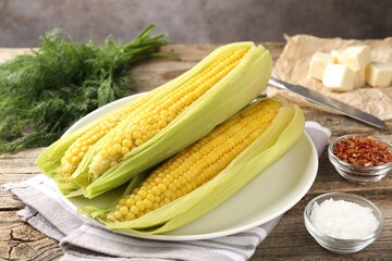 Tasty boiled corncobs, dill and spices on wooden table, closeup