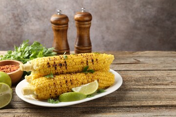Tasty grilled corncobs with parsley and lime slices on wooden table. Space for text