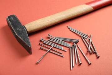 Metal nails and hammer on coral background, closeup