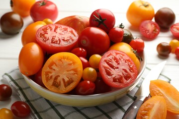 Different ripe tomatoes and knife on white wooden table, closeup