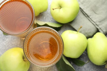 Delicious cider in glasses, apples and leaves on grey textured table, flat lay