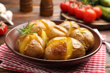 Tasty baked potatoes with rosemary served on wooden table, closeup