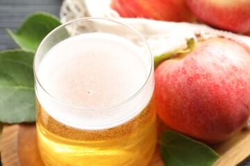 Fresh cider in glass, apples and green leaves on table, closeup