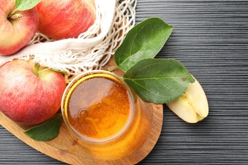 Fresh cider in glass, apples and green leaves on black textured table, flat lay