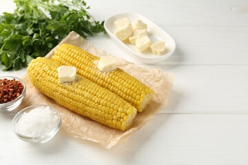 Tasty boiled corncobs with butter, spices and parsley on white wooden table