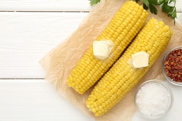 Tasty boiled corncobs with butter, parsley and spices on white wooden table, flat lay. Space for text