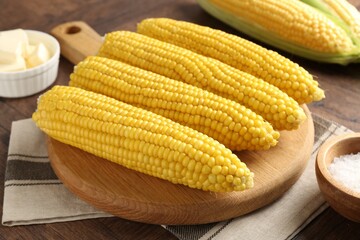 Tasty boiled corncobs, salt and butter on wooden table, closeup