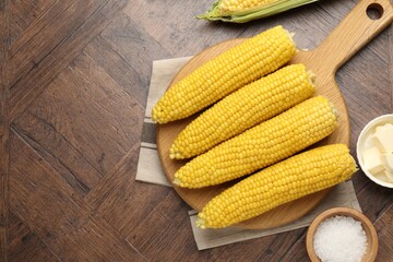 Tasty boiled corncobs, salt and butter on wooden table, flat lay. Space for text
