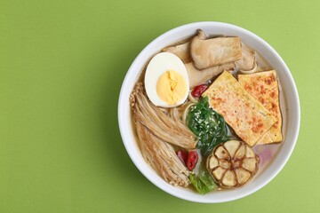 Tasty ramen with enoki and king oyster (eryngii) mushrooms on green background, top view. Space for text