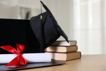 Graduation cap, laptop, diploma and books on wooden table indoors, closeup. Space for text