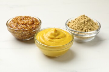 Different types of mustard on white marble table, closeup