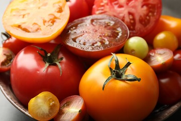 Different ripe tomatoes in bowl on grey table, closeup