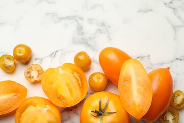 Whole and cut yellow tomatoes on white marble table, flat lay. Space for text