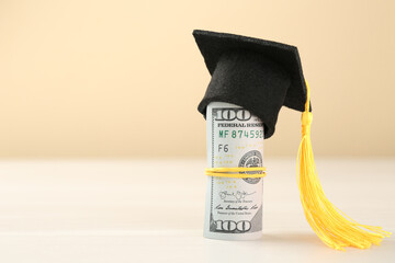 Scholarship. Graduate hat and dollar banknotes on white table against beige background, closeup....