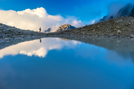 A person stands on rocky terrain, gazing at a stunning turquoise mountain lake surrounded. Dressed in hiking gear and holding trekking poles. Wildsee Pizol, Switzerland. - Powered by Adobe
