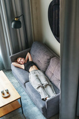 Casual lifestyle scene of girl lying on couch in modern apartment, relaxing mood.