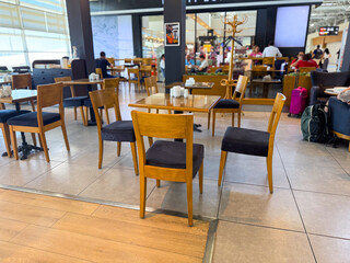 Wooden chairs and tables arranged in a public cafe area. Social interaction, leisure and travel atmosphere with focus on waiting, dining, and hospitality experience.