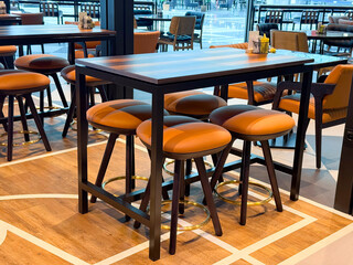Tall wooden table with leather bar stools in a public cafe area. Representation of socialization, leisure, and hospitality through travel atmosphere and lifestyle dining culture.