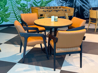 Round wooden table with leather chairs in a cafe interior near foosball game. Socialization,...