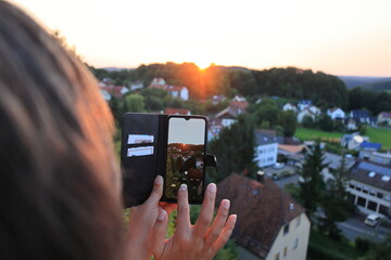 Frau fotografiert einen Sonnenuntergang mit dem Handy