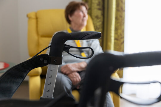 Seniorin sitzt in ihrem Zimmer im Sessel hinter ihrem Rollator