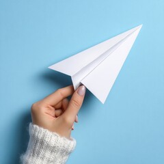 A hand delicately holding a paper airplane against a blue backdrop. The image evokes a sense of aspiration, freedom, and the pursuit of dreams
