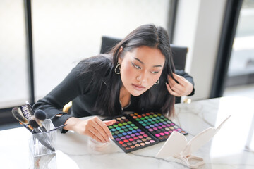 Attractive Asian female beauty influencer 
woman vlogger applying makeup recording make-up tutorial on smart phone.